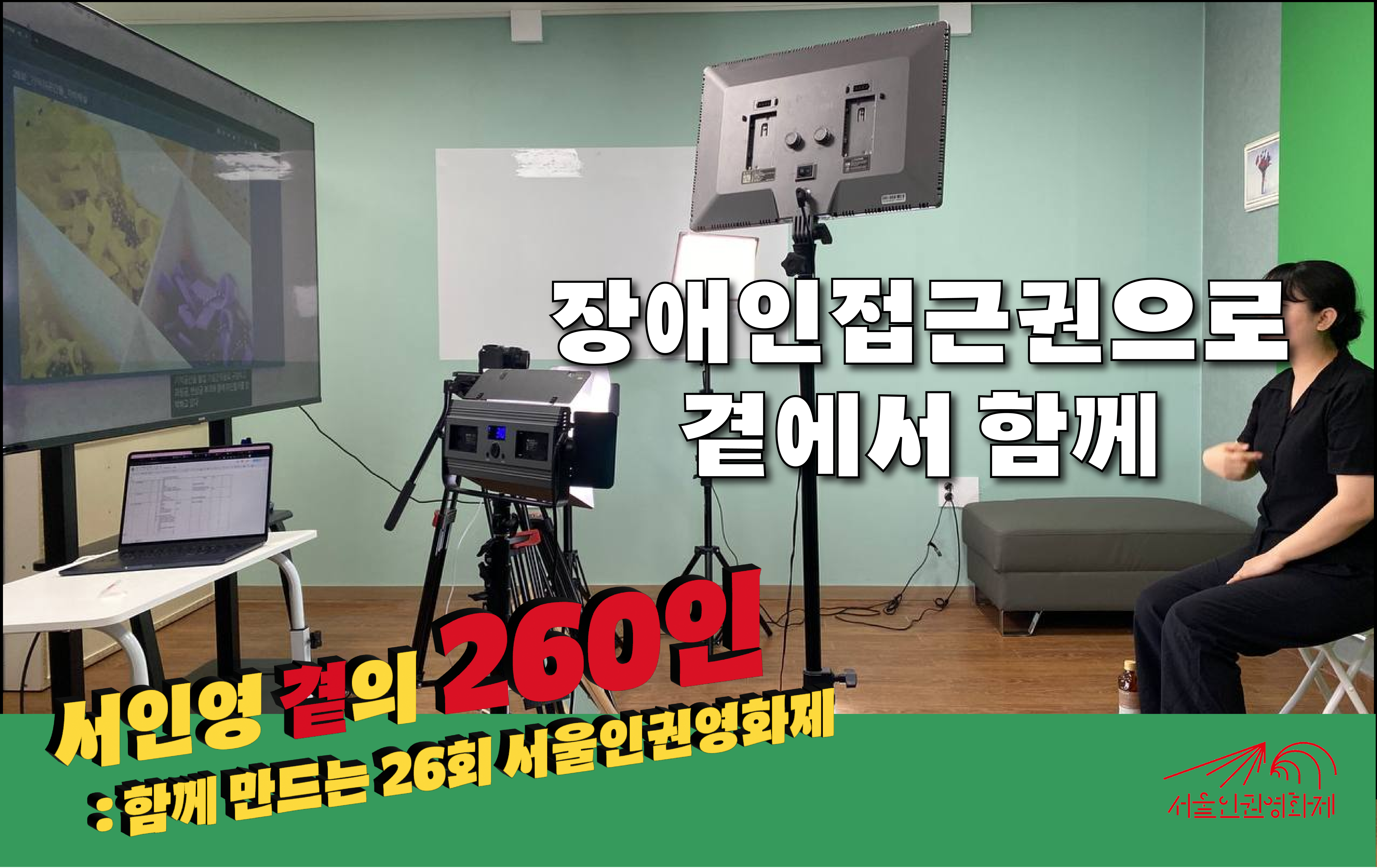 [사진] 수어 통역사가 대형 TV를 보며 수어통역을 녹화하는 장면이다. 사진 왼쪽 편에는 커다란 TV가 있다. TV에는 영화가 나오고 있다. 사진 오른쪽 편에 수어통역사가 앉아있다. 여러 개의 조명이 수어통역사를 비추고 있다. 수어 통역사 등 뒤로 녹색 스크린이 있다. 